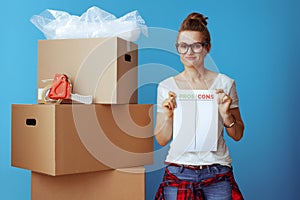 Doubting woman near cardboard box with pros cons list on blue