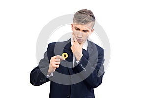 Doubting young attractive businessman trader holding bitcoin cryptocurrency, isolated on white