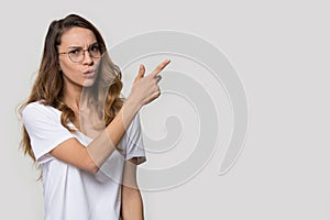 Doubting young woman wearing glasses pointing finger at copy space