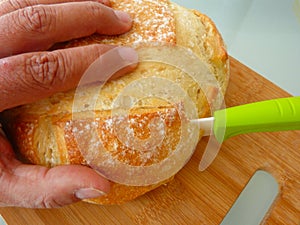 Dough bread slicing close-up view with make hand and green handle ceramic knife