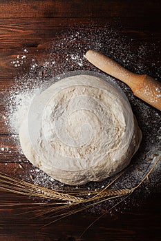 Dough with flour, rolling pin, wheat ears on rustic wooden table top view. Homemade pastry for bread or pizza. Bakery background.