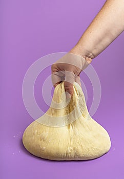 Dough isolated on a purple table. Woman stretching uncooked dough