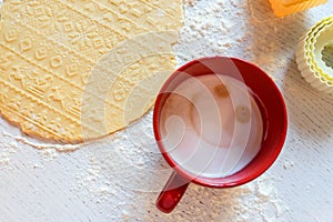 The dough with the New Year`s pattern is rolled out on the table, next to it are cookie cutters and a red mug with coffee. Concep