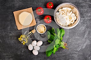 Dough, oil, cheese, tomatoes, eggs, greens over grey wooden background