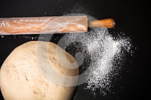 Dough, rolling pin and flour on a black background