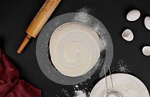Dough and rolling pin, flour on black background top view