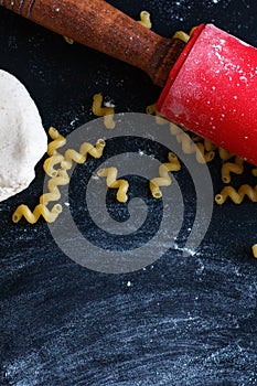 Dough, rolling pin, flour and pasta on the black table. Top view