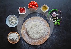 Dough and a set of pizza ingredients on a black table. Production of Italian pizza Margarita. Stage of production.