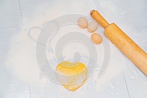 dough in the shape of a heart, flour and eggs on the table.