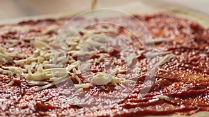 The dough is spread with tomato sauce and sprinkled with shredded cheese.