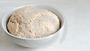 Dough from whole wheat flour in a gray bowl on a gray background. The process of making bread at home.