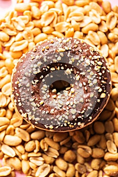 Doughnut with chocolate glaze and peanuts on a pink background. Top view