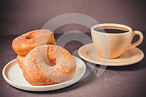 Doughnuts in a plate and a cup of black coffee. Selective focus. Dark background