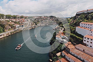 Douro river and boats swimming in it with a bridge and Porto city in the background on a cloudy day