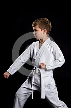 Down fist hit, pose in karate. Kid in kimono on the black background