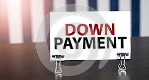 DOWN PAYMENT sign on paper on dark desk in sunlight. Blue and white background