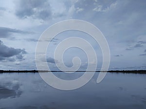 Down the river with shadows in the water and clouds above in the blue sky with some trees in the middle of the image