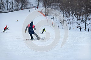 Down slope on snow covered mountain. Back view of snowboarder riding on slope, blurred selective focus