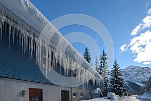 Down spout of snowy house roof with lot of icicles