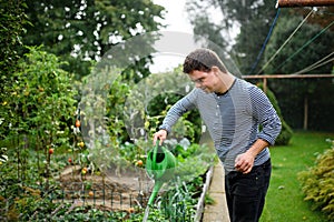 Down syndrome adult man watering plants outdoors in vegetable garden, gardening concept.