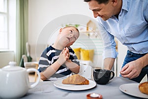 Down syndrome boy with father at the table, having breakfast.