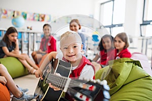 A down-syndrome boy with school kids and teacher sitting in class, playing guitar.