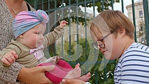 Down syndrome boy touches examines baby toddler feet. Acquaintance new