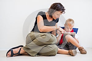 A down-syndrome school boy sitting on the floor with teacher, using tablet.