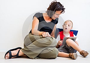 A down-syndrome school boy sitting on the floor with teacher, using tablet.