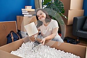 Down syndrome woman smiling confident unboxing package at new home