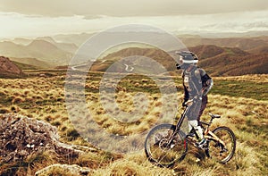 Downhill rider on a mountain bike in a mountain bike rides along the road in nature against the backdrop of the mountain