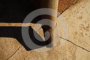 Downpipe at the corner of the building, cracks in the blind area of the house, sunlight and shadow from the drain pipe