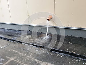 Downpipe on the facade of a modern building. heavy rain, water flows out of the downspout onto the sidewalk.