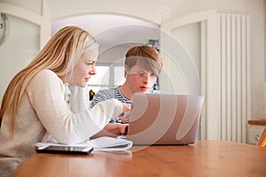 Downs Syndrome Man Sitting With Home Tutor Using Laptop For Lesson At Home