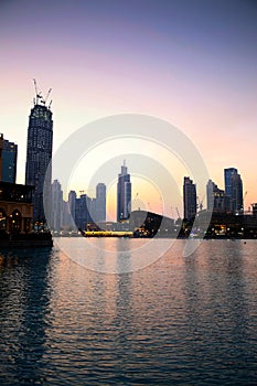 Downtown in the city at sunset with all the skyscrapers illuminated and reflecting in the lake, Dubai, United Arab Emirates