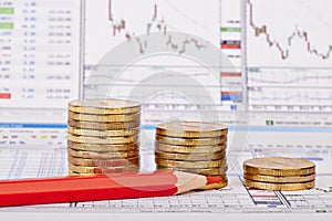 Downtrend coins stacks, red pencil, financial chart as background, red pencil. Selective focus