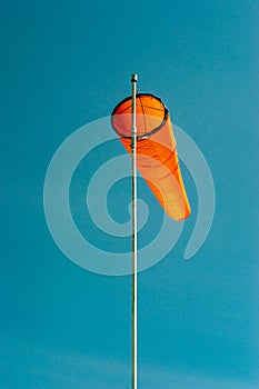 Downward angled plain orange windsock against a clear blue sky.