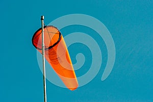 Downward angled plain orange windsock against a clear blue sky.