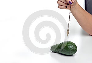 Dowser with hand-held pendulum checks the usefulness of avocado fruit. photo