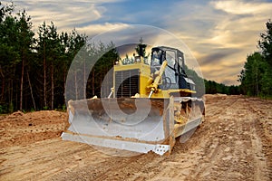 Dozer during clearing forest for construction new road. Bulldozer at forestry work on sunset background. Earth-moving equipment at