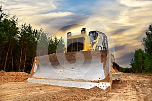 Dozer during clearing forest for construction new road. Bulldozer at forestry work on sunset background. Earth-moving equipment at