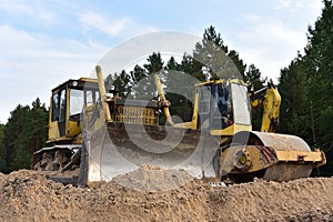 Dozer and Vibro Roller Soil Compactor at road construction and bridge projects in forest area. Heavy machinery for road work.