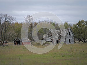 Drab Abandoned Dilapidated Farm House and Shed with clouds