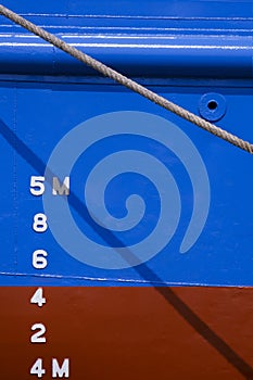 Draft mark numbers on side of blue and red rust proof vessel hull behind the old giant fiber rope in vertical frame