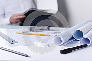 Draftsman at work, analyzing documents for drafting. Closeup of graph papers, rulers and other tools on the desk, engineer sitting