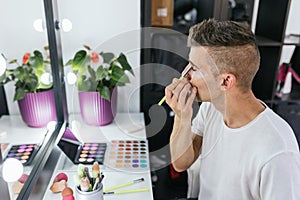 Drag queen artist applying eyeshadow while doing his makeup in the dressing room.
