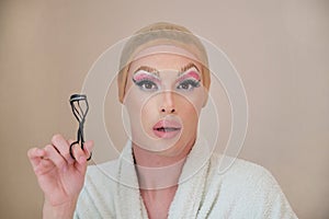 Drag queen person with a eyelash curler and wearing bathrobe looking at camera. photo