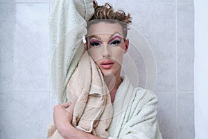 Drag queen person wearing bathrobe posing looking at camera in a bathroom.