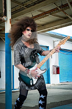 Drag queen rocker with big wig playing the guitar