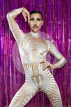Drag queen with short hair and mustache posing with fuchsia color background